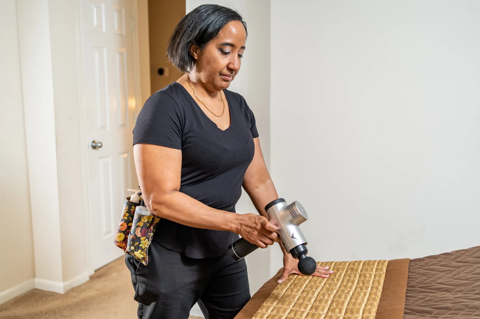 Therapist holding a Hypervolt percussion device beside a made-up massage table